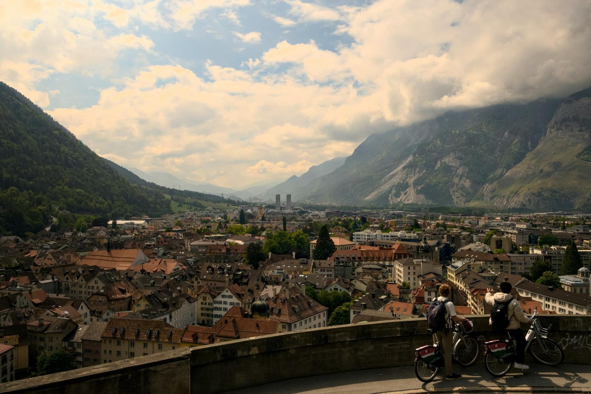 Blick über die Dächer der Churer Altstadt ins Rheintal mit Bergen und Wolken.