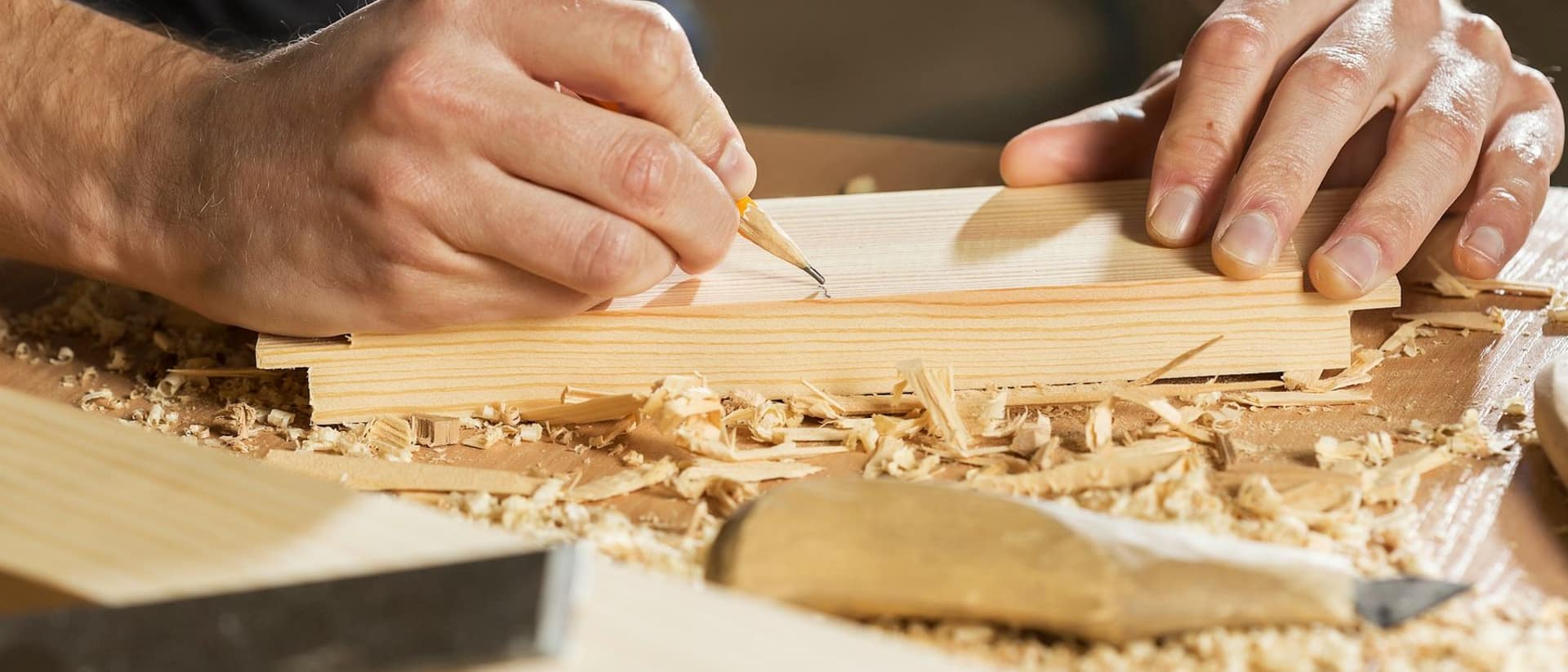 Eine Hand zeichnet mit einem Bleistift eine Linie auf ein Holzbrett.