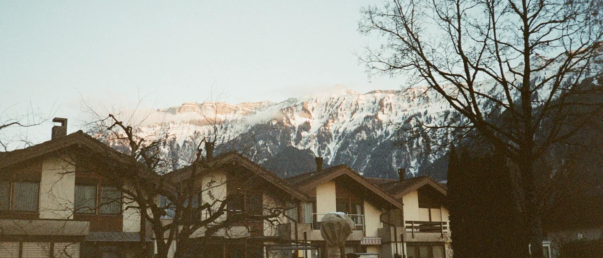 Wohnhäuser mit Giebeldächern in Interlaken im Abendlicht, dahinter verschneite Berge.