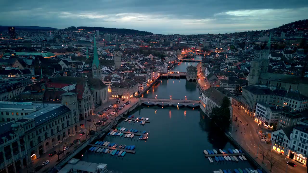 Luftaufnahme der Zürcher Altstadt an der Limmat in der Abenddämmerung, mit Fraumünster, Brücken und beleuchteten Strassen.